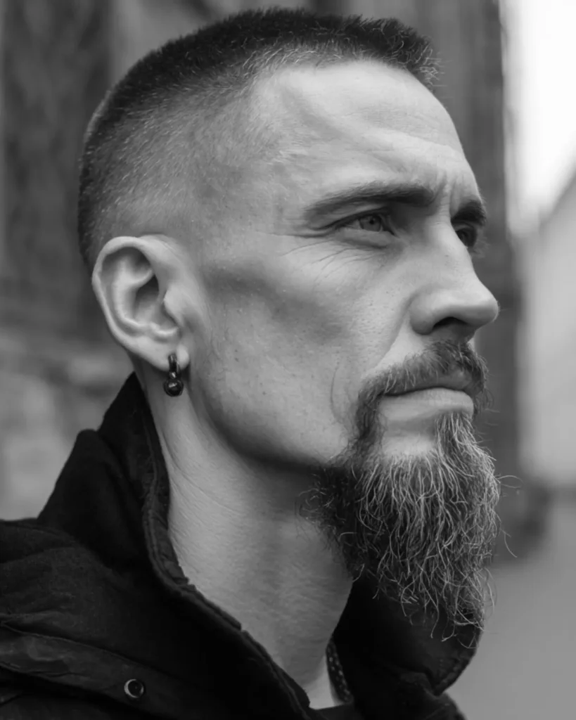 Man with a square face, extended goatee and short buzz haircut