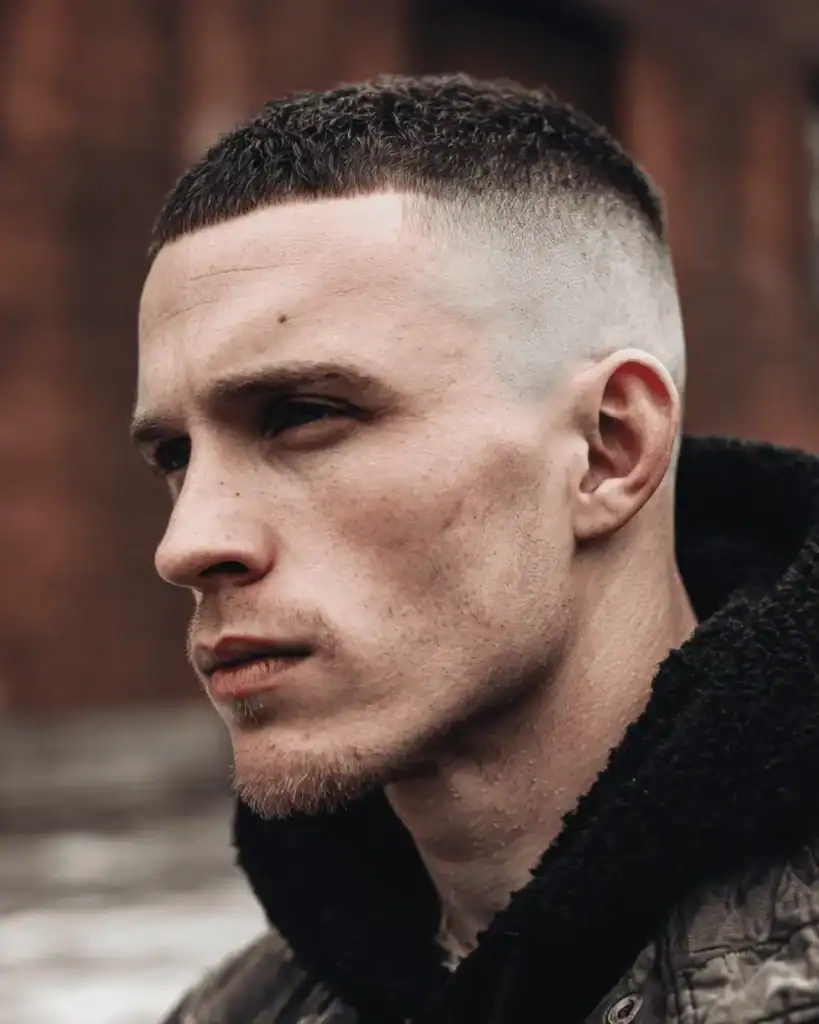 Side profile of a man with a short, textured buzz cut and a sharp high skin fade.
