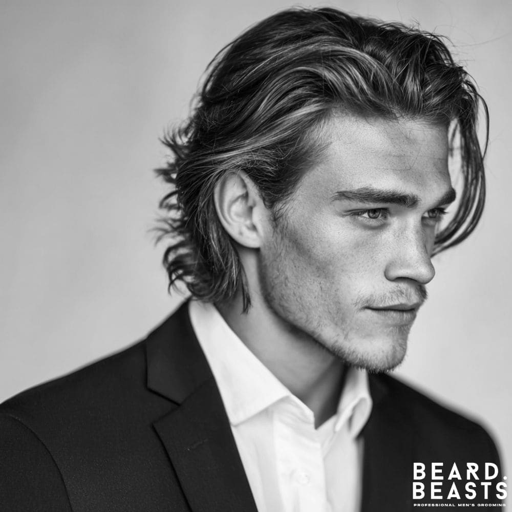 A man in a suit with a professional bro flow hairstyle, featuring medium-length wavy hair brushed back for a confident business look.