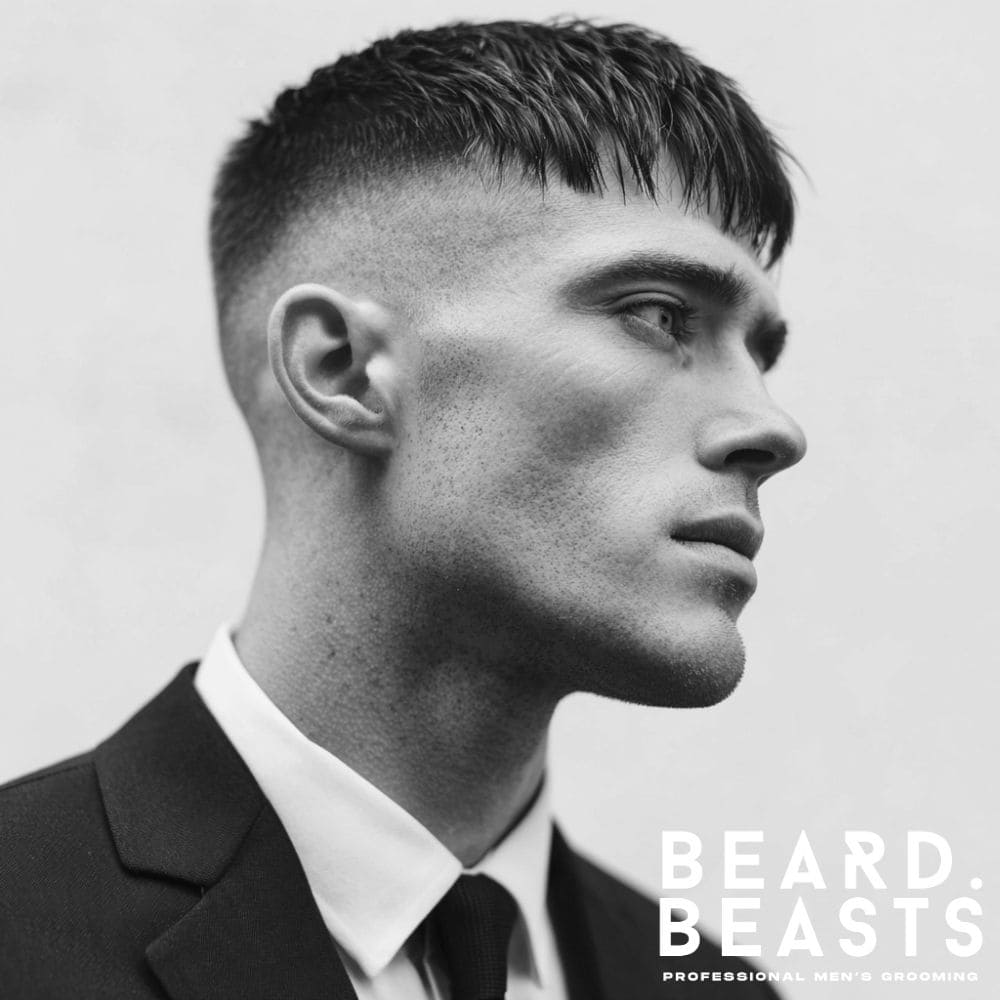 A man wearing a suit and tie with a modern French crop, featuring a high fade and a sharp, textured fringe for a professional look.