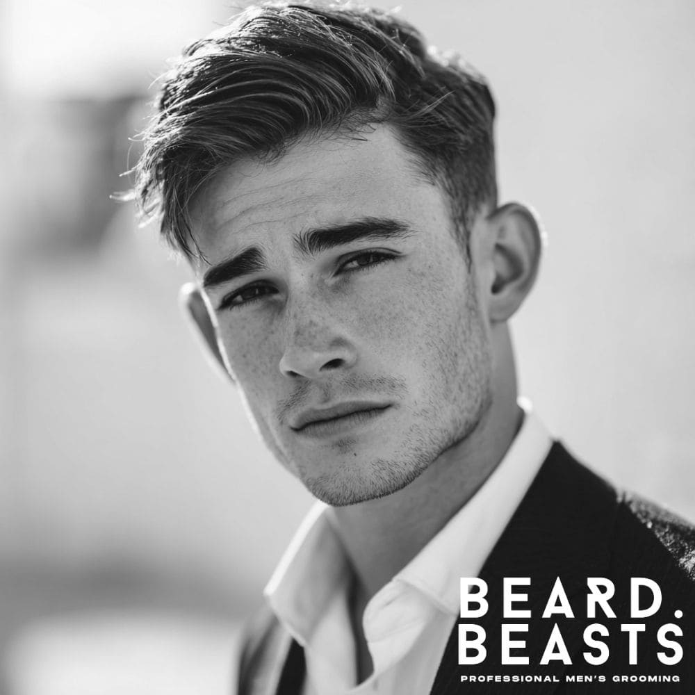 A young professional man with a classic Ivy League haircut, featuring a neat side part and a textured, side-swept fringe.