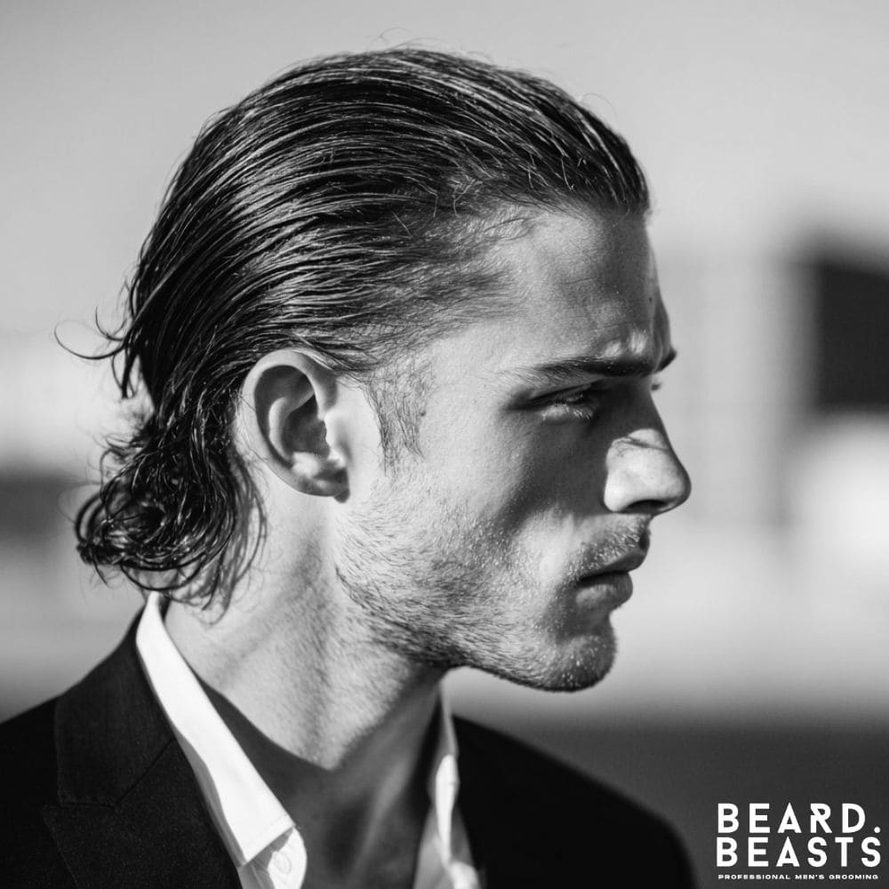 A professional man with a classic long slick back hairstyle, using pomade to create a sharp and powerful business look.