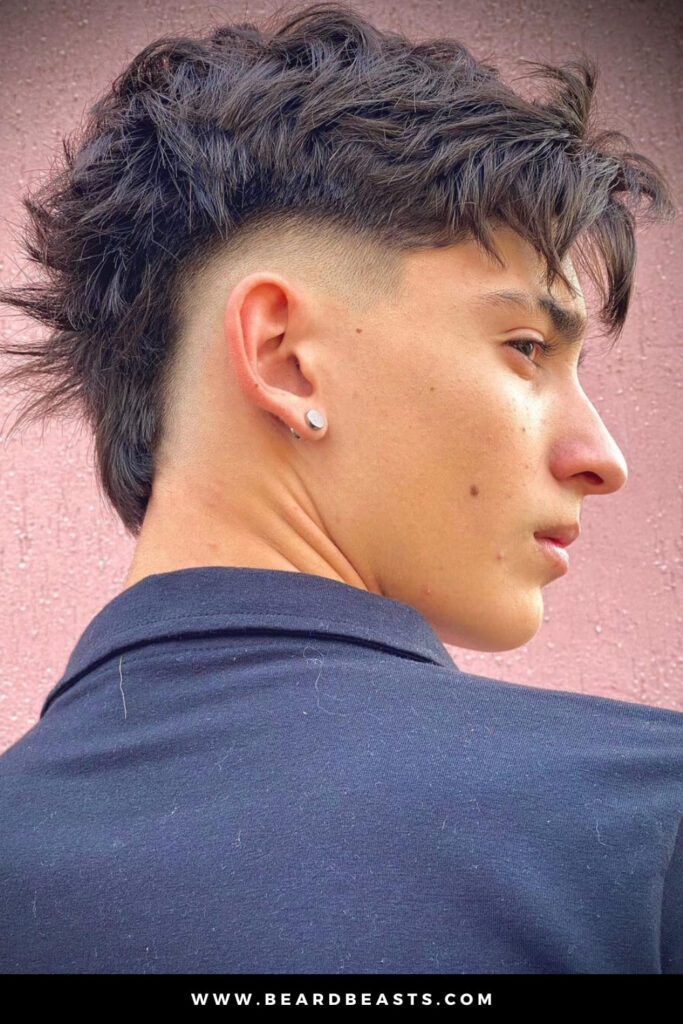 Side profile of a man with a modern mohawk haircut, featuring a textured long top and shaved short sides, creating a bold short on sides, long on top hairstyle with edgy contrast.