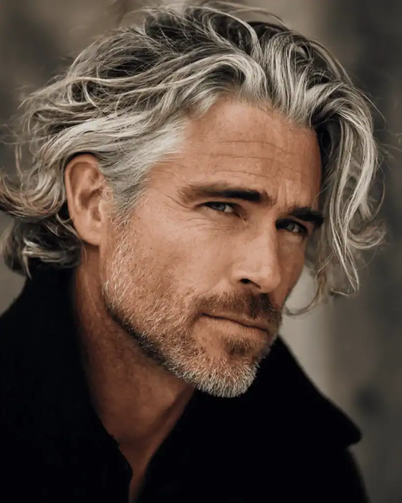 A portrait of a handsome older man with a Bro Flow hairstyle, featuring medium-length wavy silver hair swept back naturally for a relaxed, confident look.