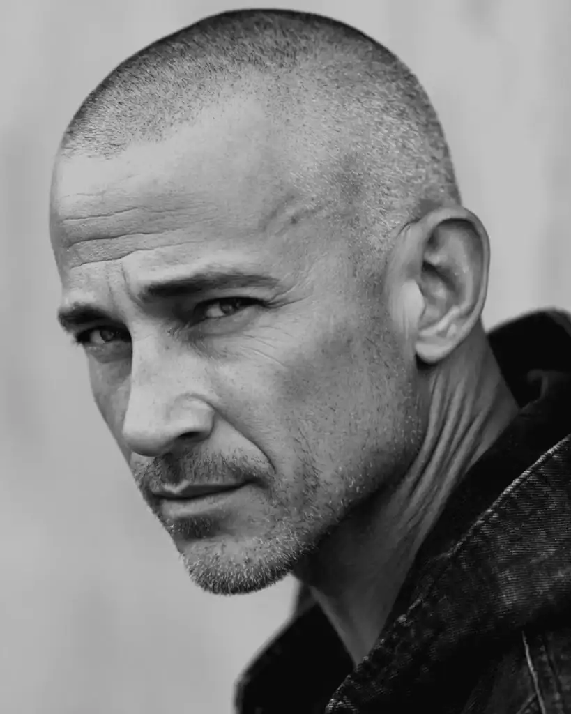 A close-up portrait of an older man with a buzz cut hairstyle, featuring hair clipped short and even for a low-maintenance, masculine look that works well for thinning hair.
