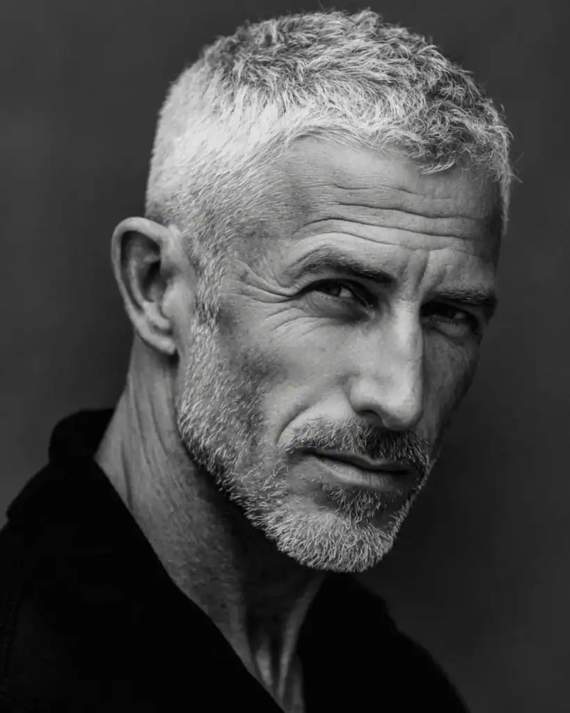 A portrait of a confident older man with a crew cut hairstyle, featuring short sides and slightly longer, textured silver hair on top for a neat and timeless look.