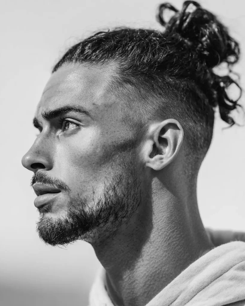 man bun with high fade haircut, curly top and skin fade sides, side profile