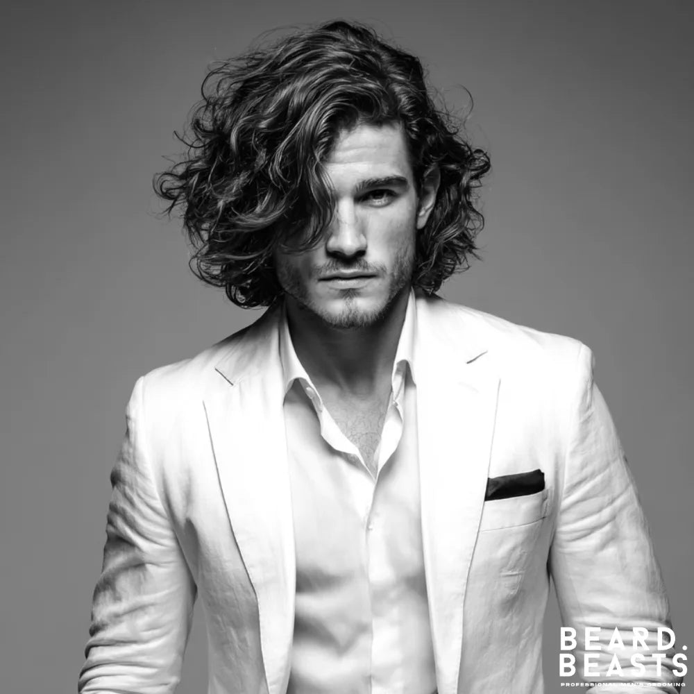 Long, tousled curls styled with a deep side part offer a sophisticated option for a modern professional, as shown on this man in a white suit.