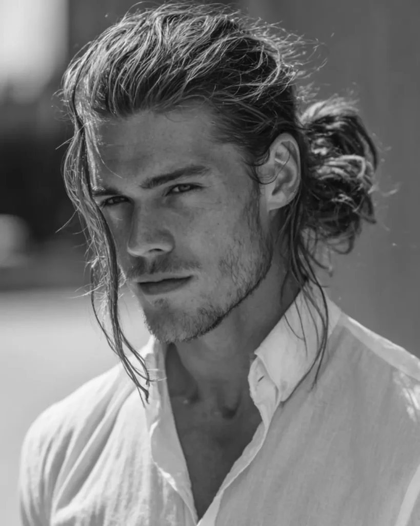 Loose tied-back long hair with face-framing strands and height at the crown, showing a long hairstyle option for men with round faces.