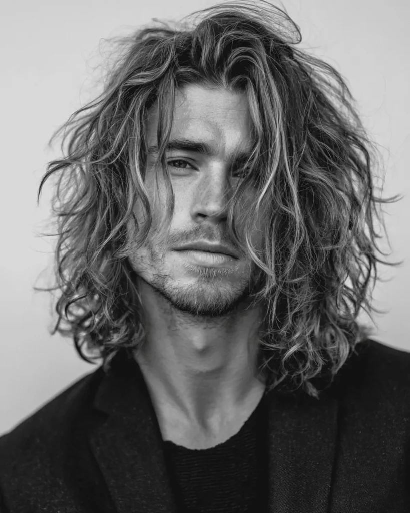 Black and white portrait of a man with a long shaggy hairstyle featuring flowing layers and natural wavy texture