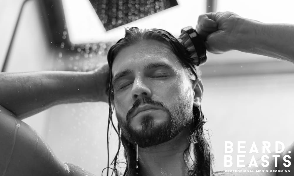 Man with long hair massaging his scalp in the shower, representing a healthy hair care routine for maintaining strong, clean hair.