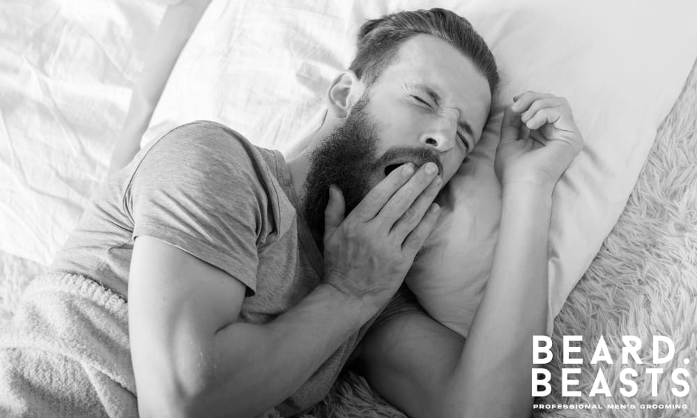 Man yawning in bed with his hair tied back, illustrating a common grooming mistake.