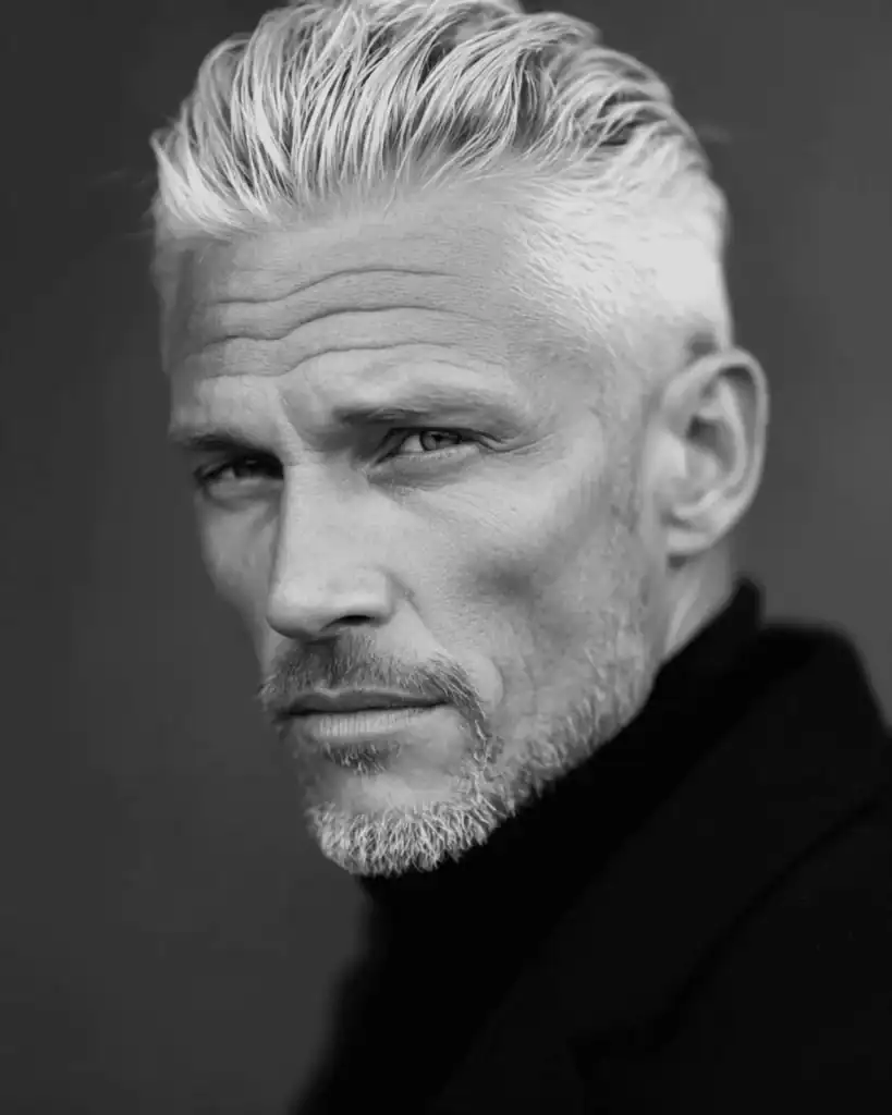 A black and white portrait of a sophisticated older man with a medium length slick back hairstyle, featuring silver hair brushed smoothly back for a commanding, professional look.