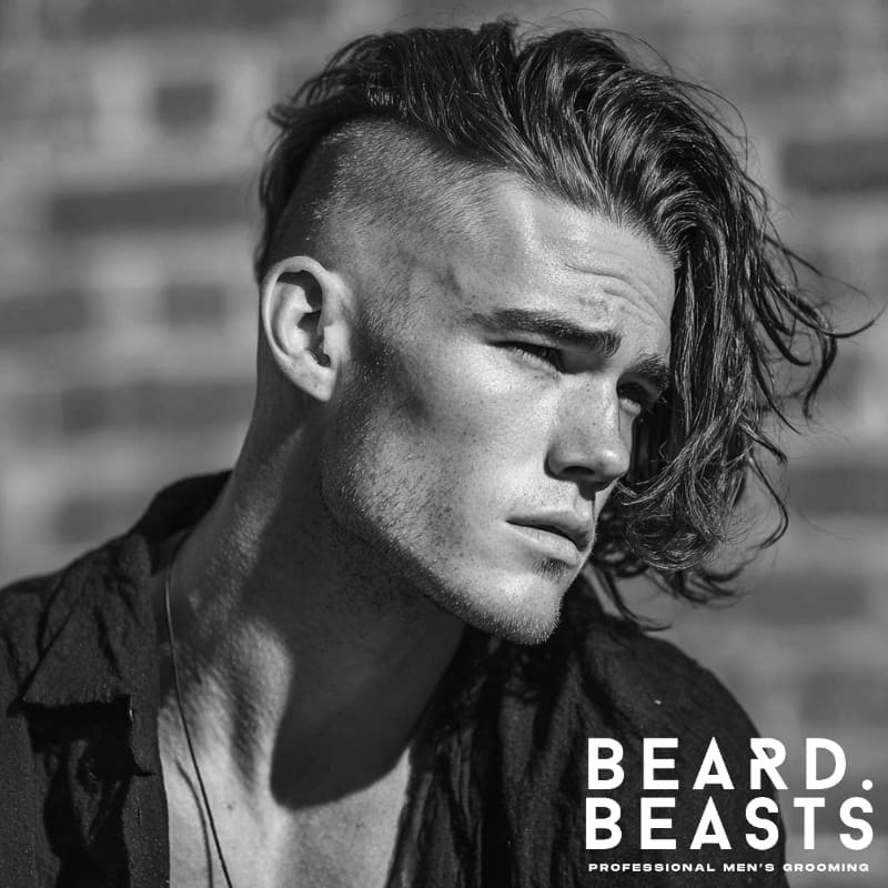 Man with a high skin fade and long hair styled to one side, showcasing a bold short on sides, long on top haircut with sharp contrast and modern edge.