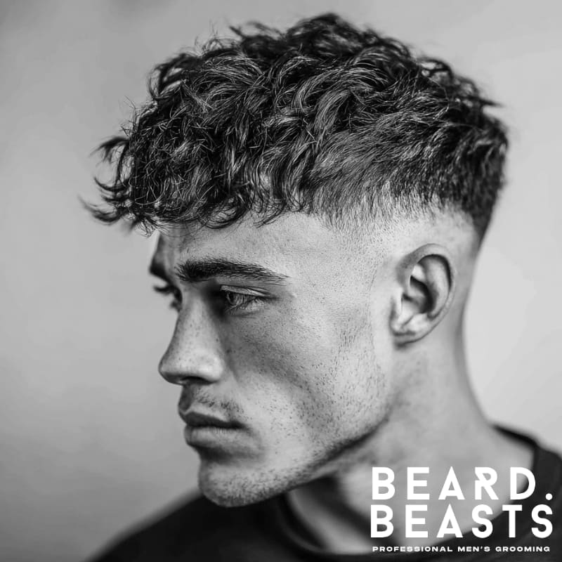 Man with textured curls on top and a faded short sides haircut, showcasing a modern short on sides, long on top style that highlights natural curls with sharp contrast.