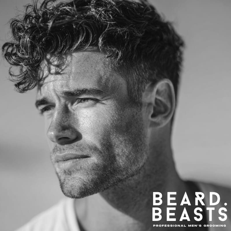 Close-up of a male model with a wavy textured crop haircut, featuring short sides and natural curly texture on top, for a modern surfer look.
