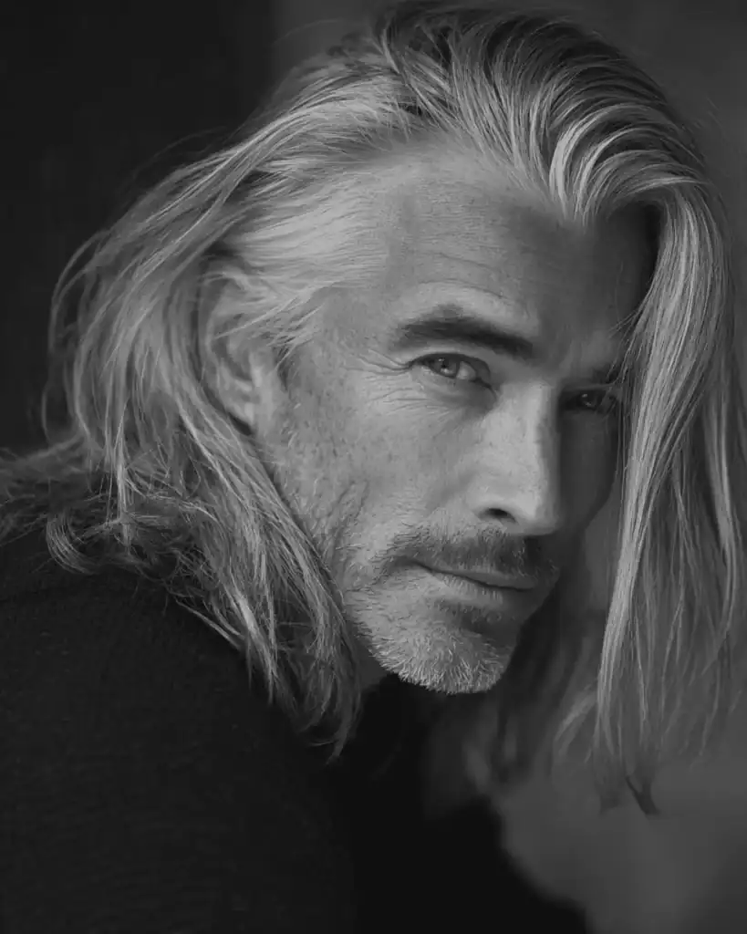 A close-up portrait of a charismatic older man with a Silver Fox hairstyle, featuring healthy, metallic silver hair and a confident expression.