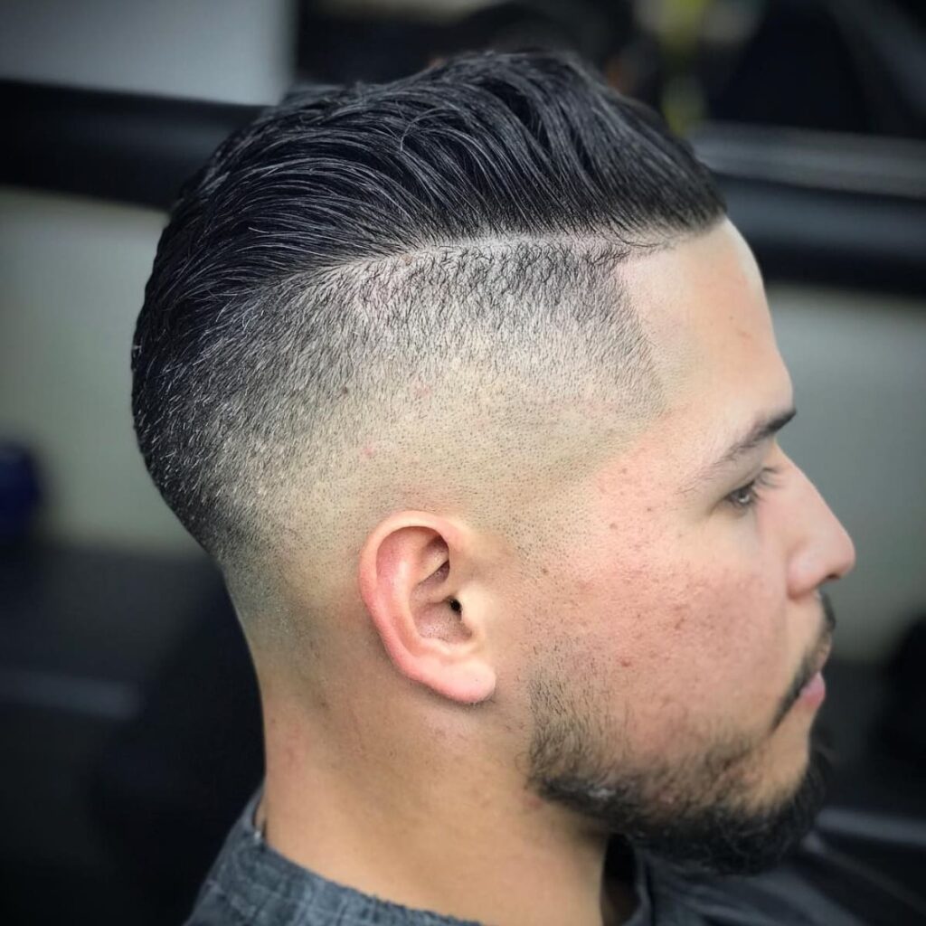 Side profile of a man with an undercut hairstyle featuring sharp, clean edges. The longer top is styled back, creating a distinct contrast with the closely shaved sides, adding depth and definition to the look. The hairstyle combines a bold, edgy undercut with a modern and polished appearance.