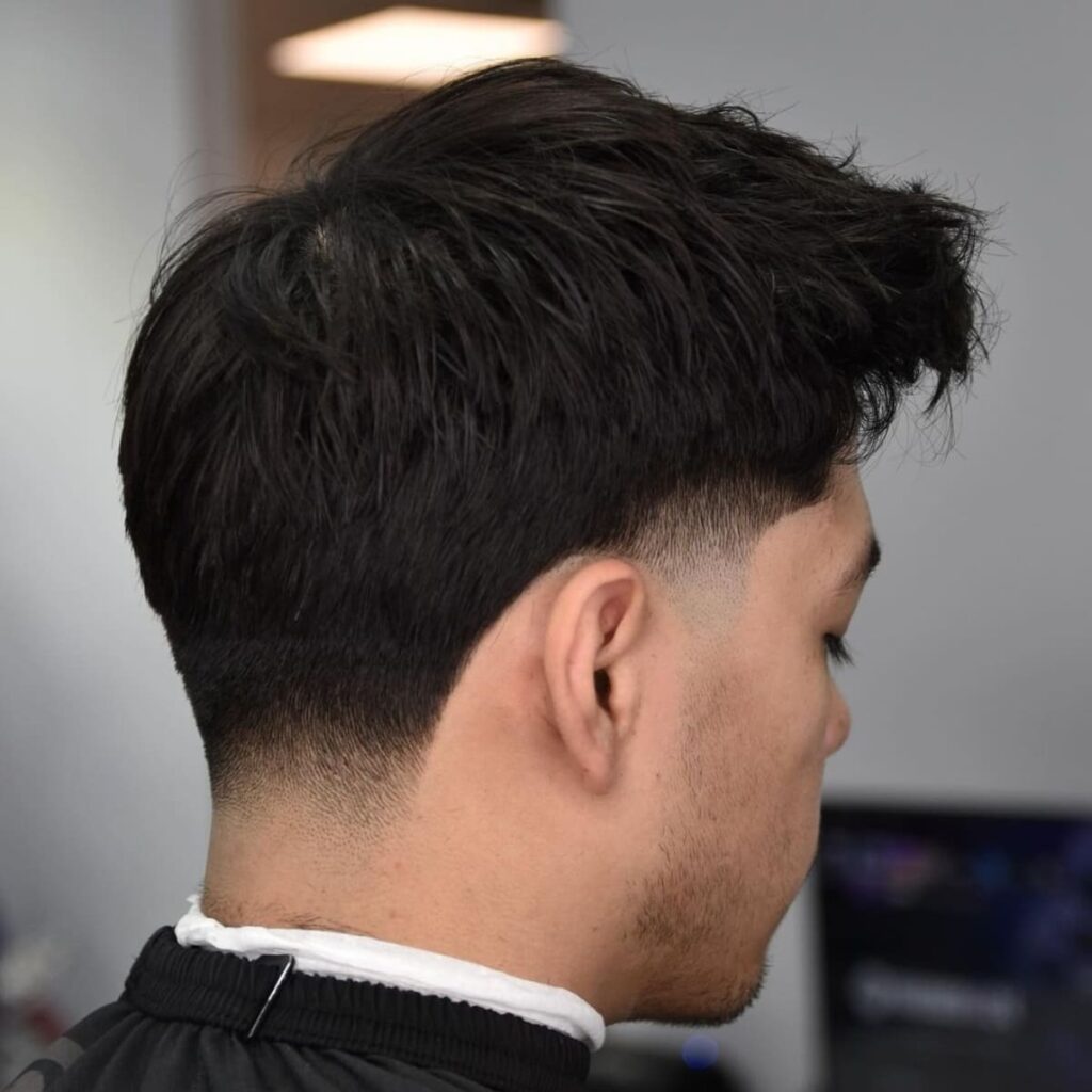 Side view of a man with a low taper, showcasing a subtle blend starting just above the ear and gently tapering down to the nape. The haircut maintains volume on top with a textured, natural look, creating a soft contrast between the longer hair and the cleanly tapered sides. This style offers a refined yet relaxed appearance, perfect for those who prefer a low-maintenance but stylish look.