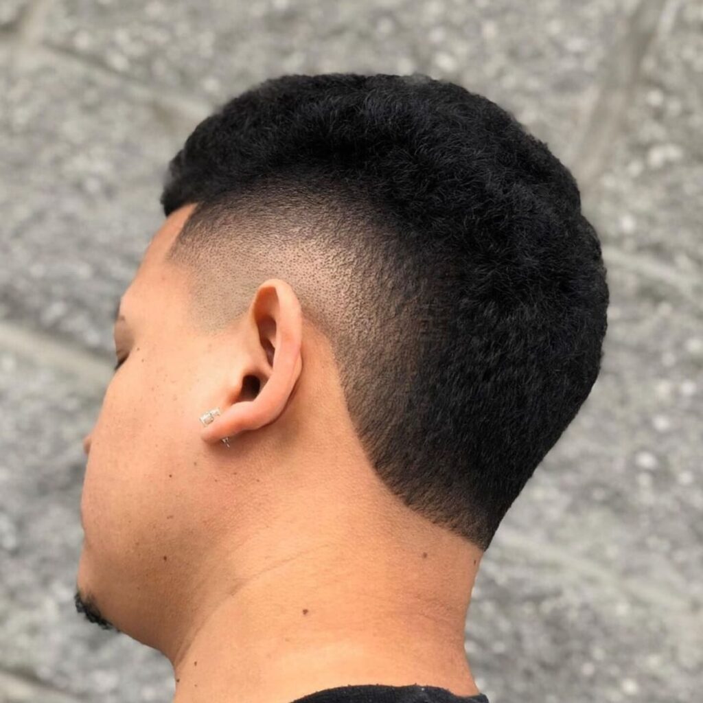 Close-up of a man with a short, classic burst fade mohawk. The clean fade circles the ear, blending into the short, textured top, creating a sharp and modern look.