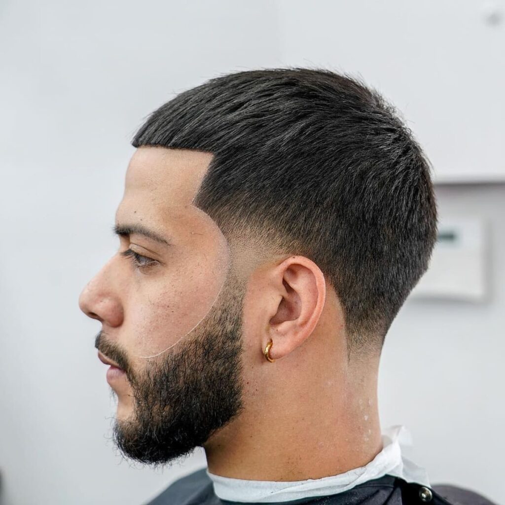 Side profile of a man with a clean and sharp French Crop with Taper Fade hairstyle. The cut features a neat, short cropped fringe and a smooth fade from the sides and back, creating a sleek and modern look. The style is paired with a well-groomed beard, enhancing the overall sharp appearance