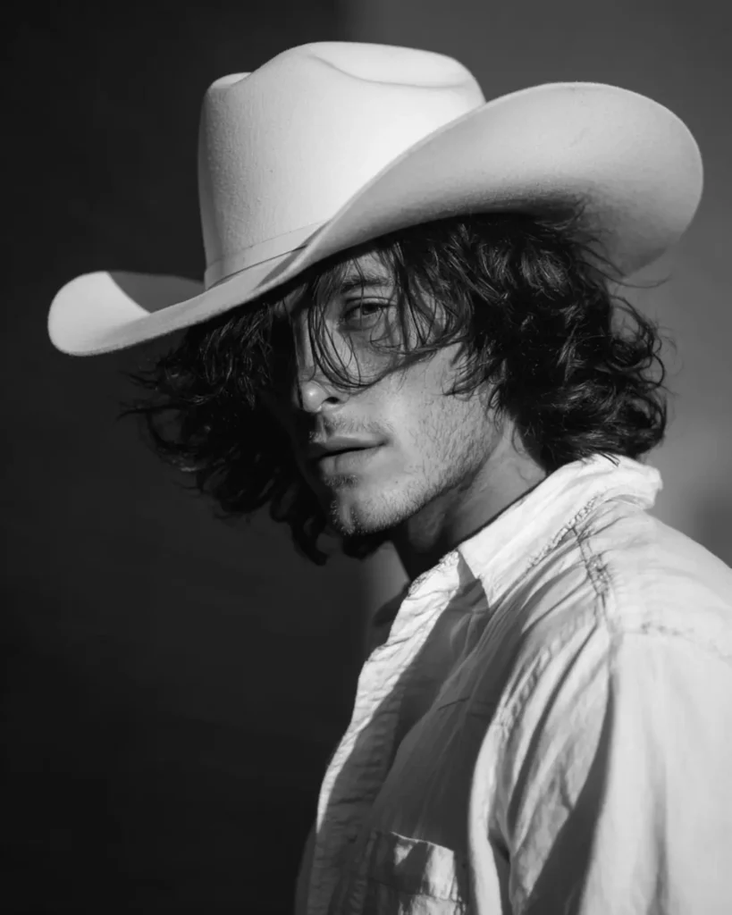 Layered shoulder-length shag cowboy haircut on a man with loose wavy hair under a cowboy hat