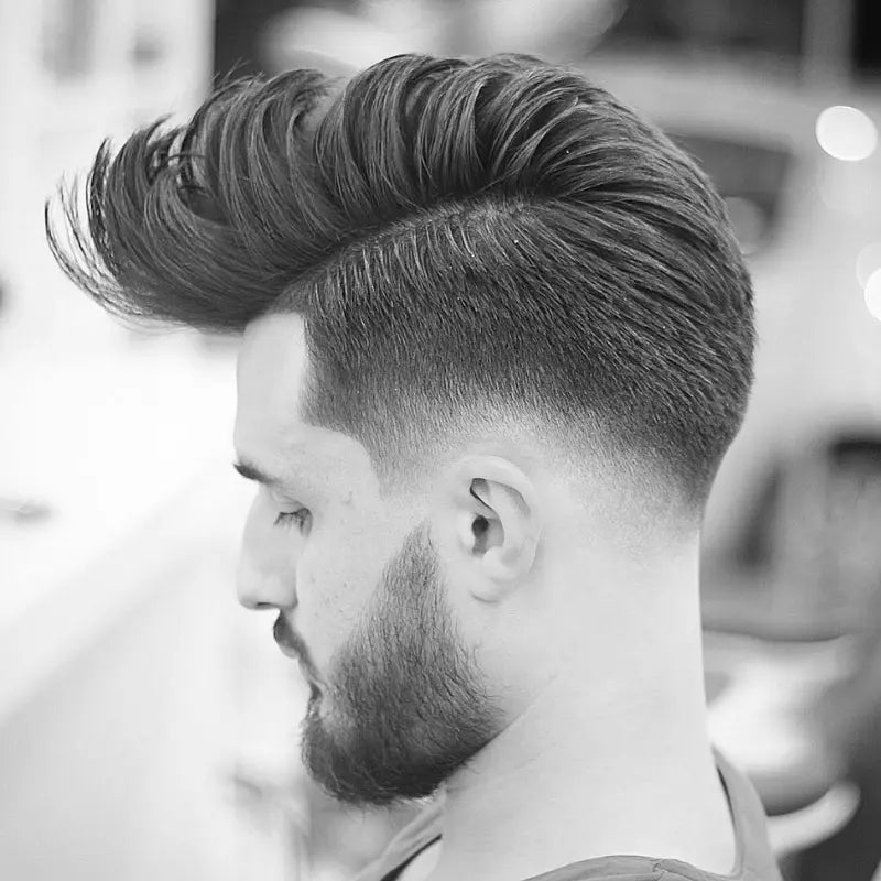 Subtle fade on the sides, voluminous top styled back for a sleek and balanced look, paired with a well-groomed beard.