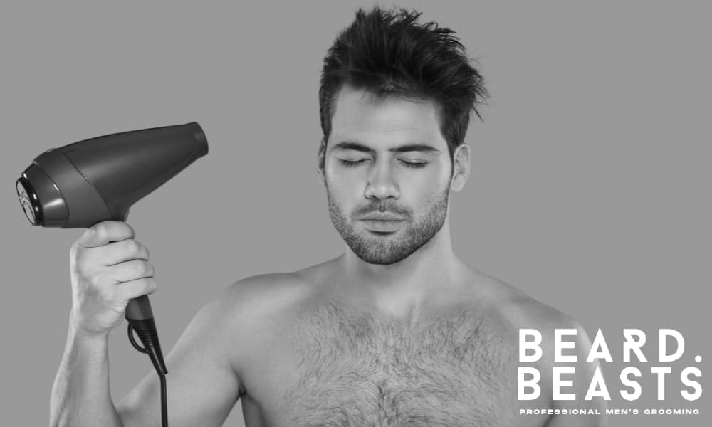 Shirtless man with closed eyes using a red hair dryer against a grey background