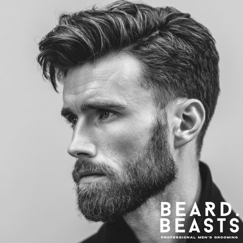 Man with a side part quiff and full beard—lifted top, soft part, and clean taper blending into facial hair.
