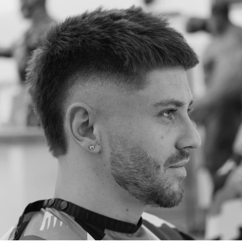 A sharp skin burst fade hairstyle featuring a clean, high contrast fade that circles the ear, creating a unique look. The top is styled with a textured finish, adding a modern flair to the classic fade.