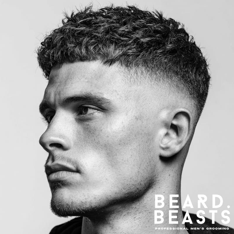 Drop skin fade hairstyle with textured curly hair on top, showcasing a clean and sharp fade that gradually drops behind the ear. A modern and fresh example of skin fade hairstyles.