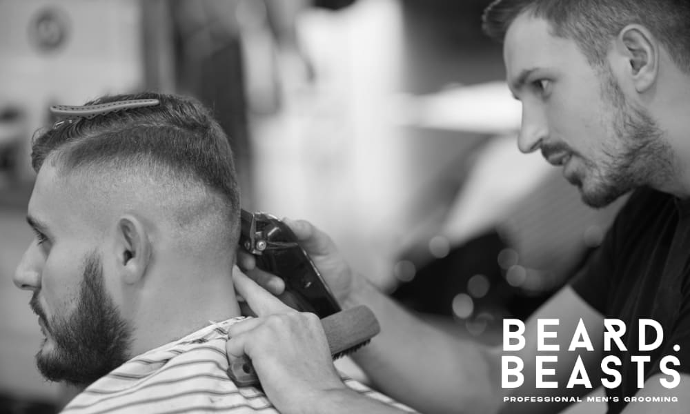 A young professional barber carefully cutting his customer's hair with clippers, focusing on the fade while the client sits in the barber chair.