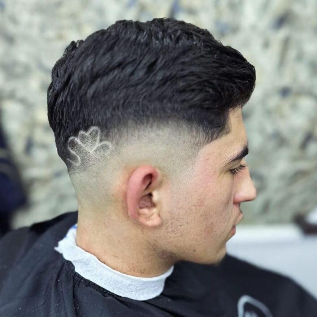 Side profile of a man showcasing a stylish fade haircut with a unique shaved design on the tapered section. The design features a creative heart-shaped pattern etched into the fade, adding a bold and artistic touch.