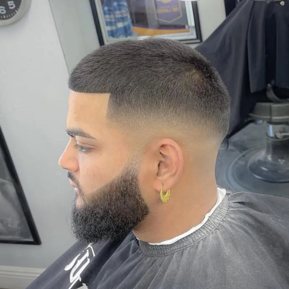 Man with a mid skin fade buzz cut and full beard, featuring sharp faded sides and a thick beard for bold contrast and definition.