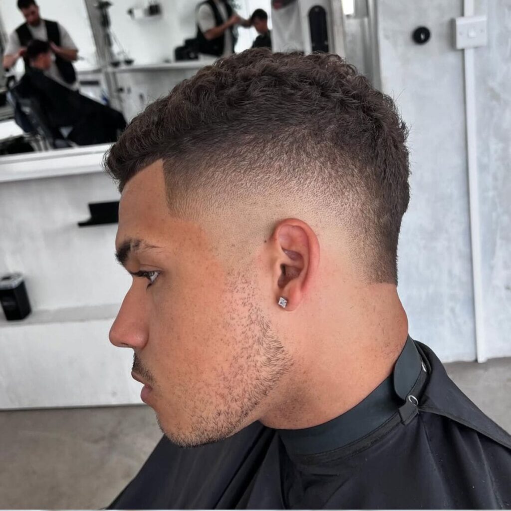 Curly short hair burst fade with a sharp rounded fade around the ears and clean edge up, modern men’s hairstyle 2025.