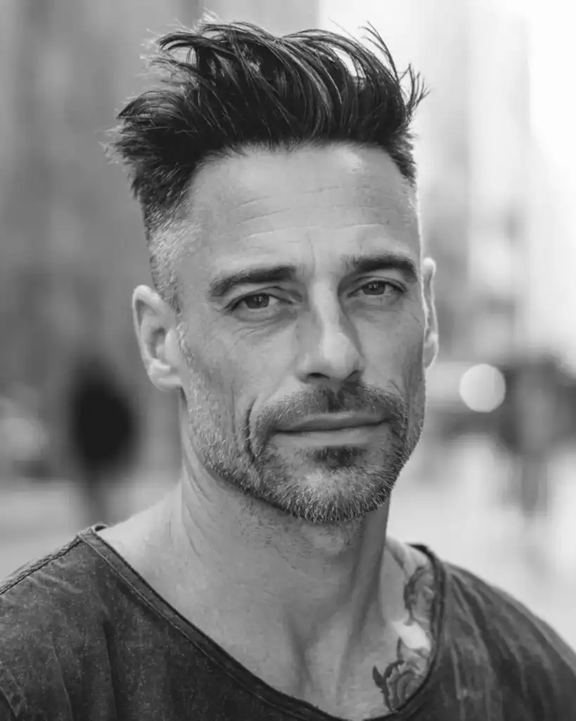 Portrait of a man over 40 with a brush up hairstyle, featuring hair styled straight upward with a textured, matte finish.