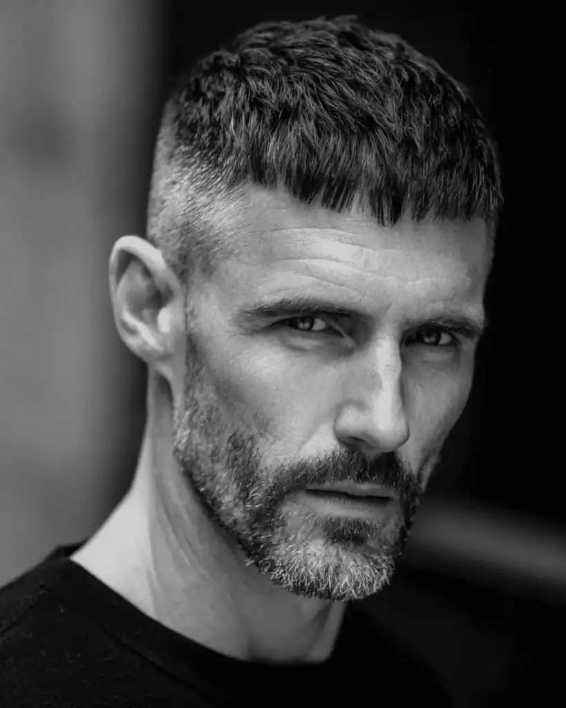 Portrait of a serious man over 40 with a classic Caesar cut, featuring a short, blunt fringe brushed forward to create a horizontal line.