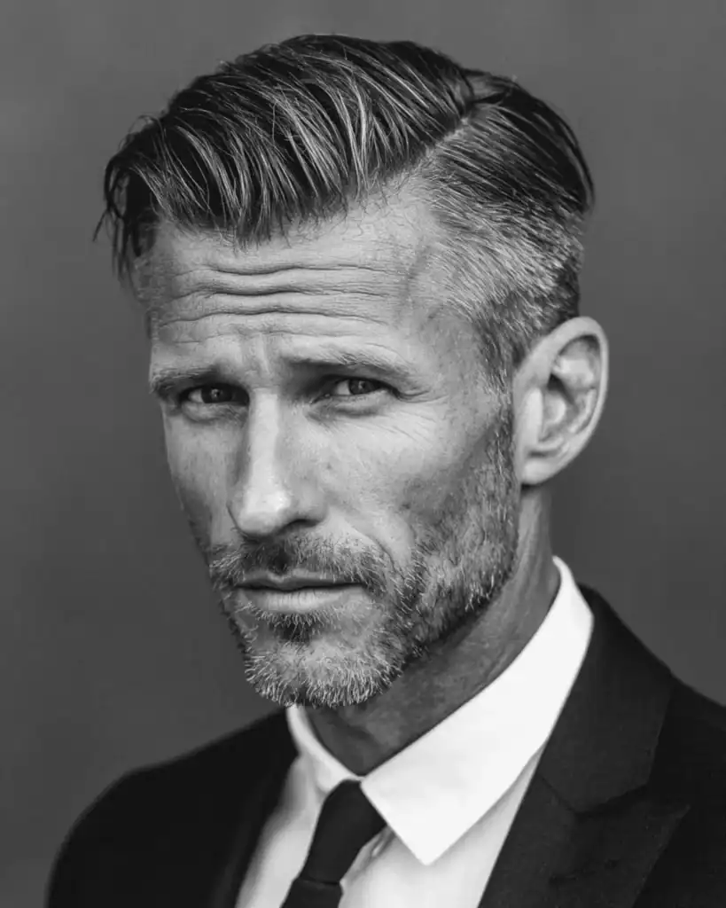 Black and white portrait of a professional man over 40 with a classic side part hairstyle, featuring a sharp side parting and combed-over top, wearing a suit and tie.