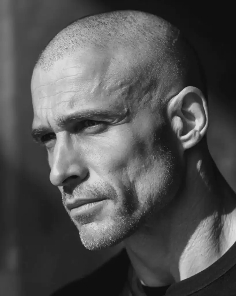 Close-up of a rugged man over 40 with an induction cut hairstyle, showing a very short #0 buzz cut that reveals head shape and bone structure