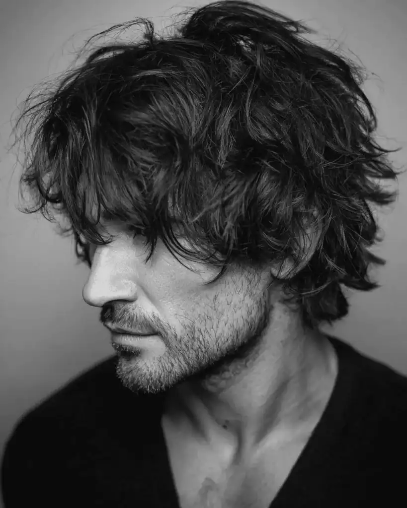 Black and white portrait of a man over 40 with a layered shag hairstyle, featuring broken layers falling over the ears and a gritty, textured finish.