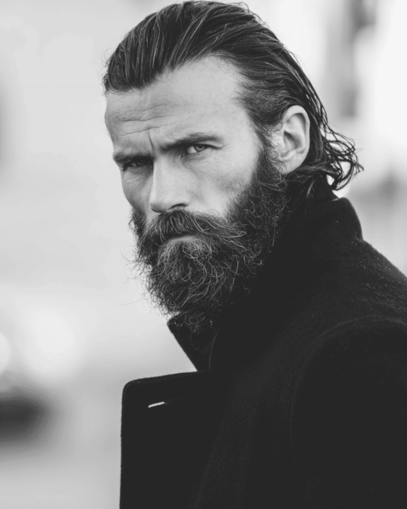 Black and white portrait of a rugged man over 40 with shoulder-length hair slicked back and a full beard.
