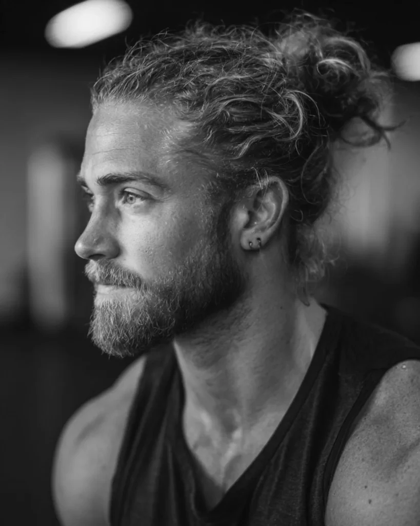 men's man bun athletic hairstyle with loose gather and beard in gym setting, side profile view