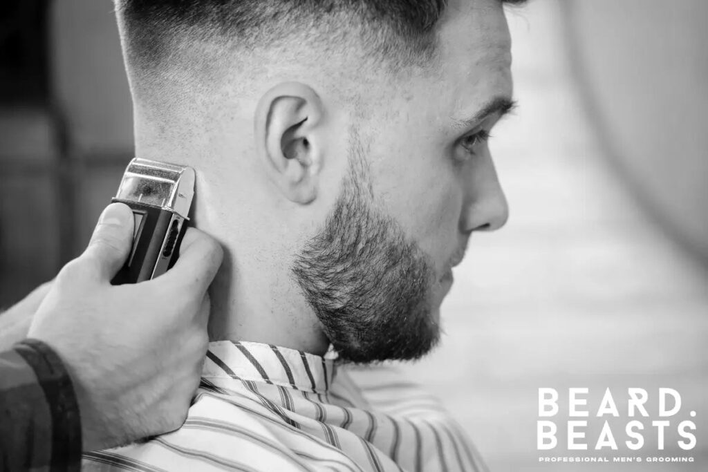 Man getting the back of his neck shaped with clippers during a haircut, wearing a barber cape, with the Beard Beasts logo in the corner.