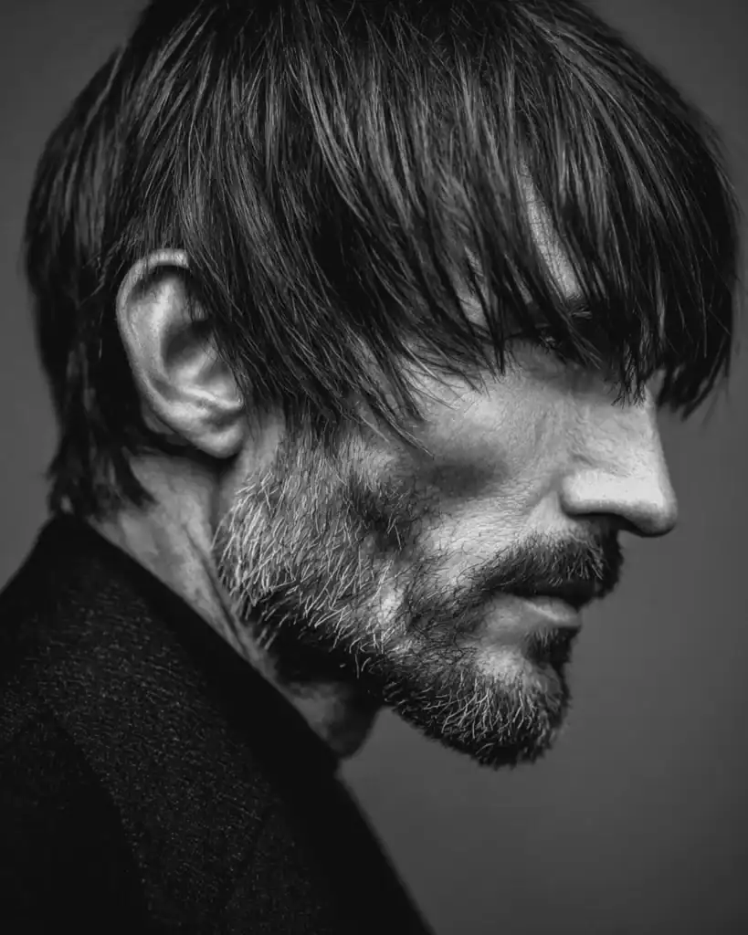 Black and white profile of a man over 40 with a modern mod cut, featuring a heavy textured fringe brushed forward and fuller sides.