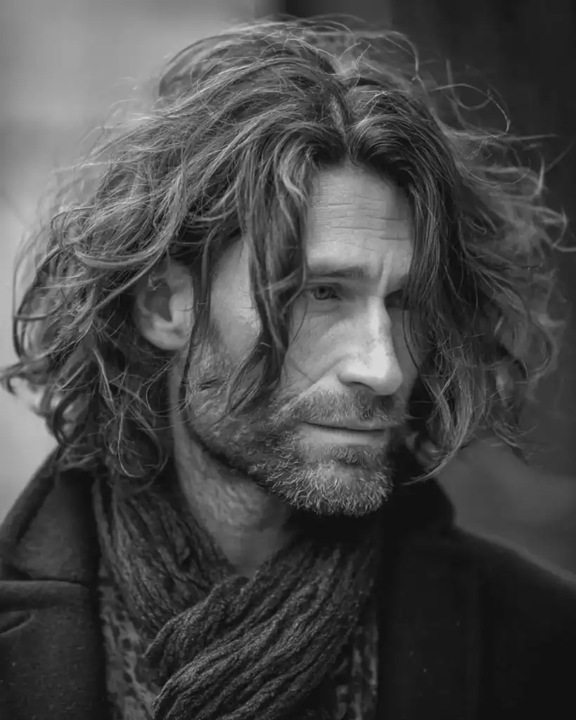 Portrait of a man over 40 with a rocker shag hairstyle, featuring mid-length wispy layers, natural waves, and a rugged, lived-in look.