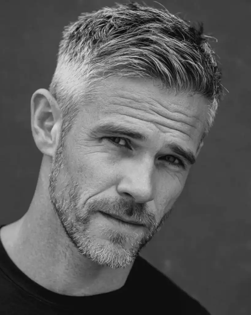 Portrait of a mature man with a short comb over hairstyle, featuring a neat diagonal sweep on top and short scissor-cut sides without a harsh fade.