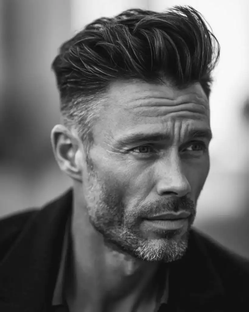 Black and white portrait of a man over 40 with a short pompadour hairstyle, featuring high volume styled upward at the front and tapered sides.