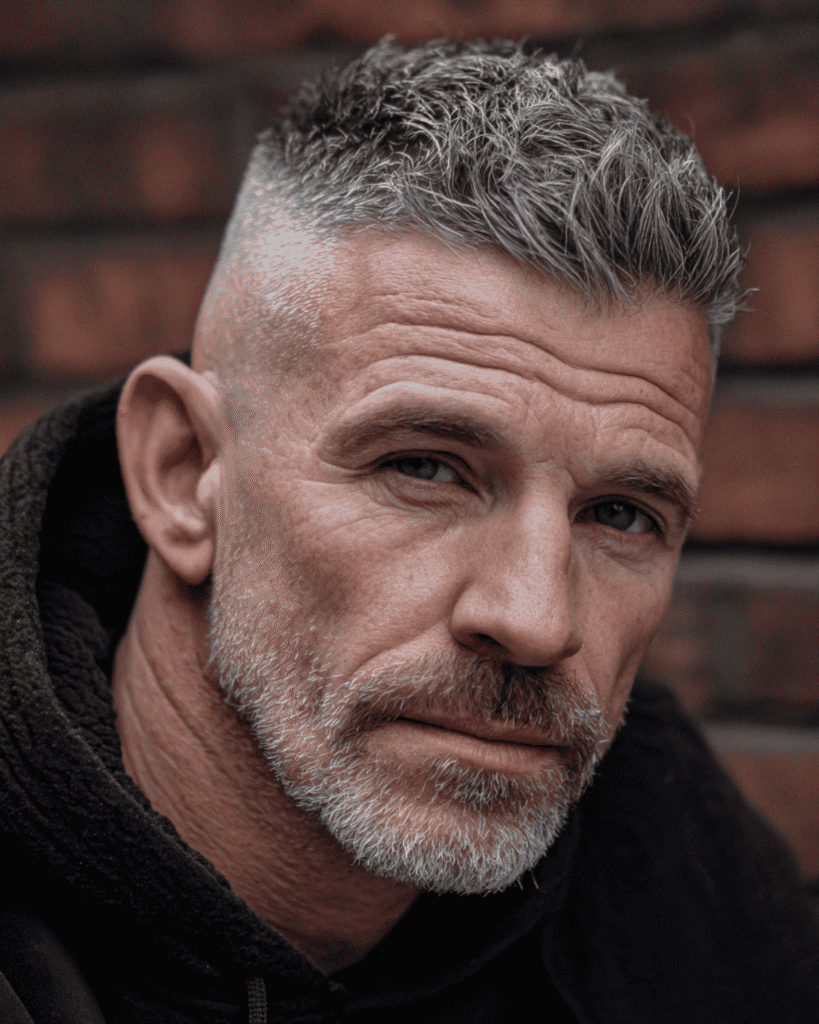 Portrait of a rugged man over 40 wearing a short textured fade, featuring tight faded sides and a choppy, messy grey top for volume.