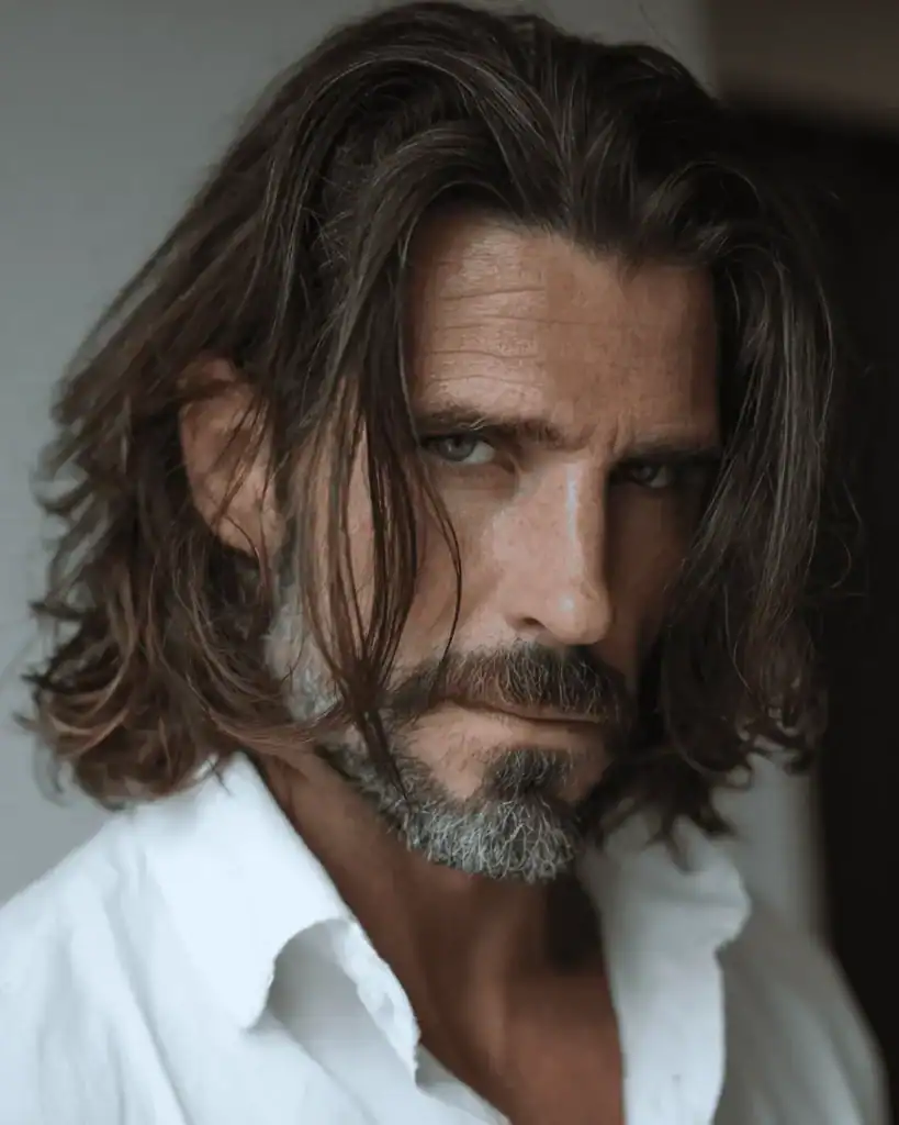 Portrait of a handsome man over 40 with a shoulder-length sweep hairstyle, featuring thick, healthy wavy hair flowing loosely back.