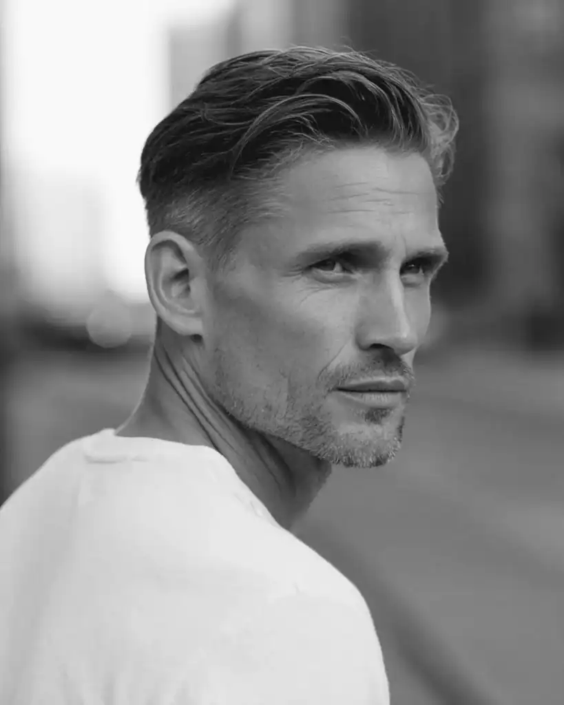 Side profile of a man over 40 with a soft swept back hairstyle, featuring longer hair brushed back with natural volume and a matte finish.